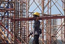 man in grey jacket and yellow hard hat standing on orange metal ladder