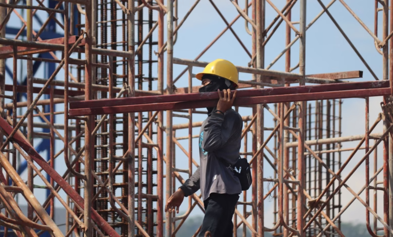 man in grey jacket and yellow hard hat standing on orange metal ladder