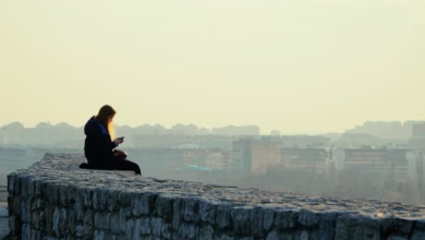woman in black jacket sitting on gray concrete wall during daytime