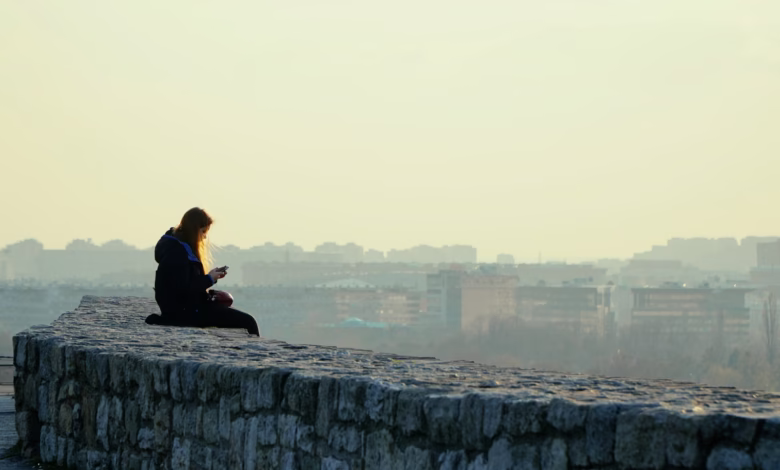 woman in black jacket sitting on gray concrete wall during daytime