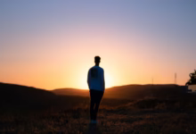 man in blue shirt standing on brown field during sunset