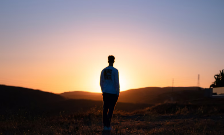 man in blue shirt standing on brown field during sunset
