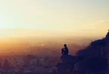 man sitting on rock formation in cliff during golden hours