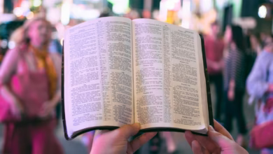 person holding bible on road with people walking on sidewalk beside buildings during nighttime
