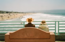 Two people sit on a bench overlooking the ocean.