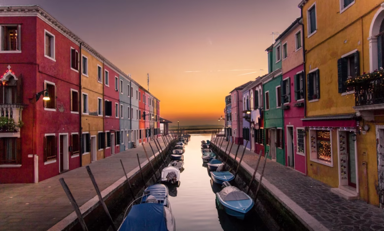 blue boats parked on river between multicolored buildings at sunset