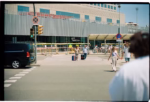 People with luggage crossing street near building.