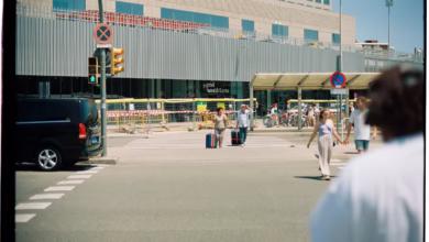 People with luggage crossing street near building.