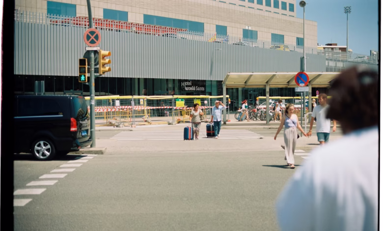 People with luggage crossing street near building.