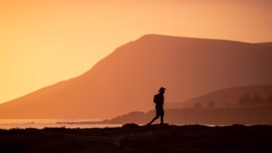 silhouette of man standing on hill during sunset