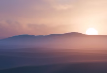 Sun setting behind hazy desert mountains at dusk