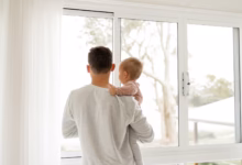 boy in gray sweater standing beside window during daytime