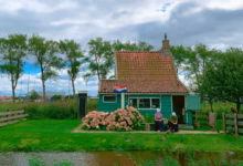Quaint green cottage with Dutch flag surrounded by nature and pink flowers.