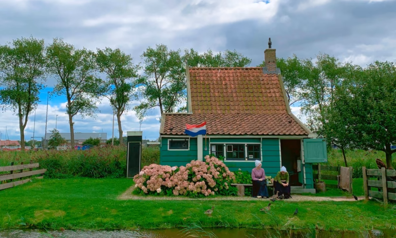 Quaint green cottage with Dutch flag surrounded by nature and pink flowers.