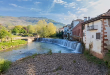 A scenic waterfall flows past charming buildings