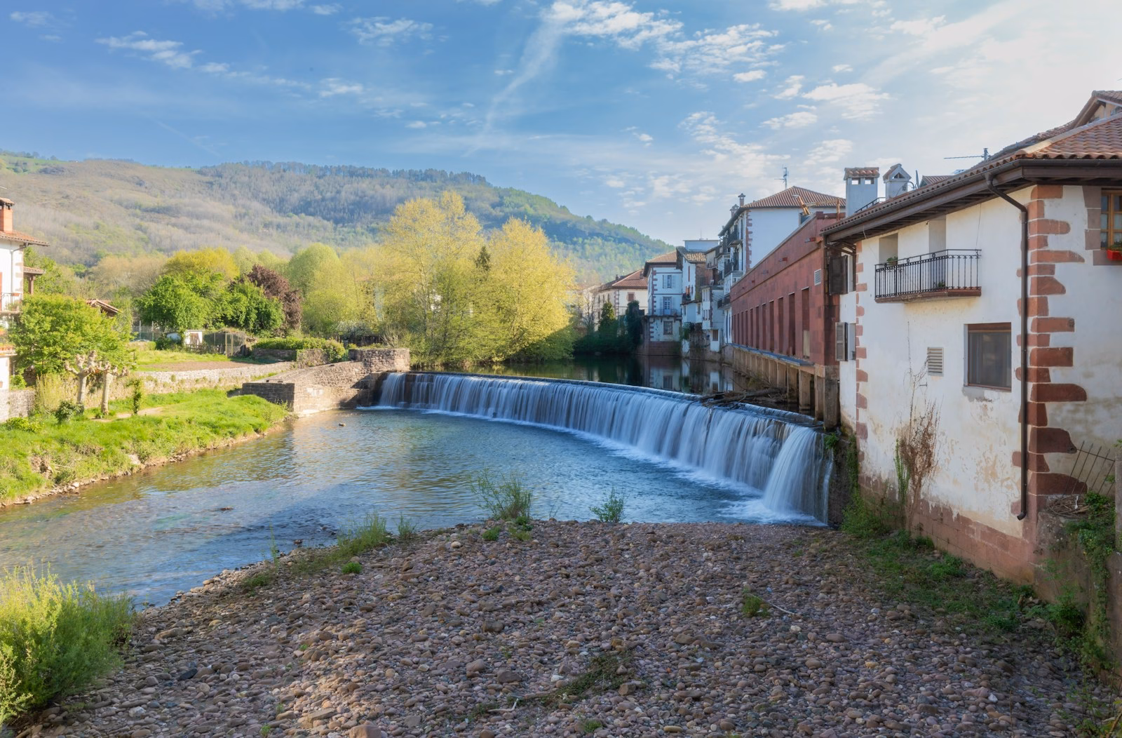 A scenic waterfall flows past charming buildings