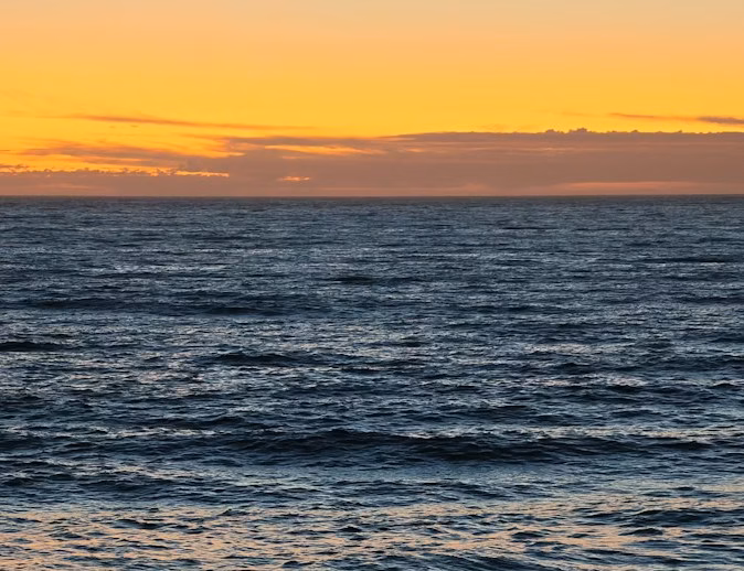 Two people in silhouette on a beach under a warm orange sky