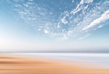 A long exposure of a sandy beach meeting the sea under a cloudy sky