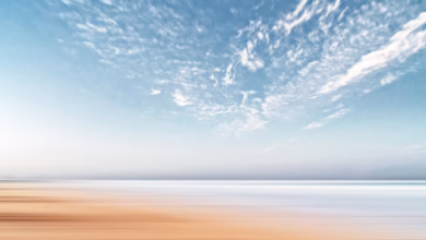 A long exposure of a sandy beach meeting the sea under a cloudy sky